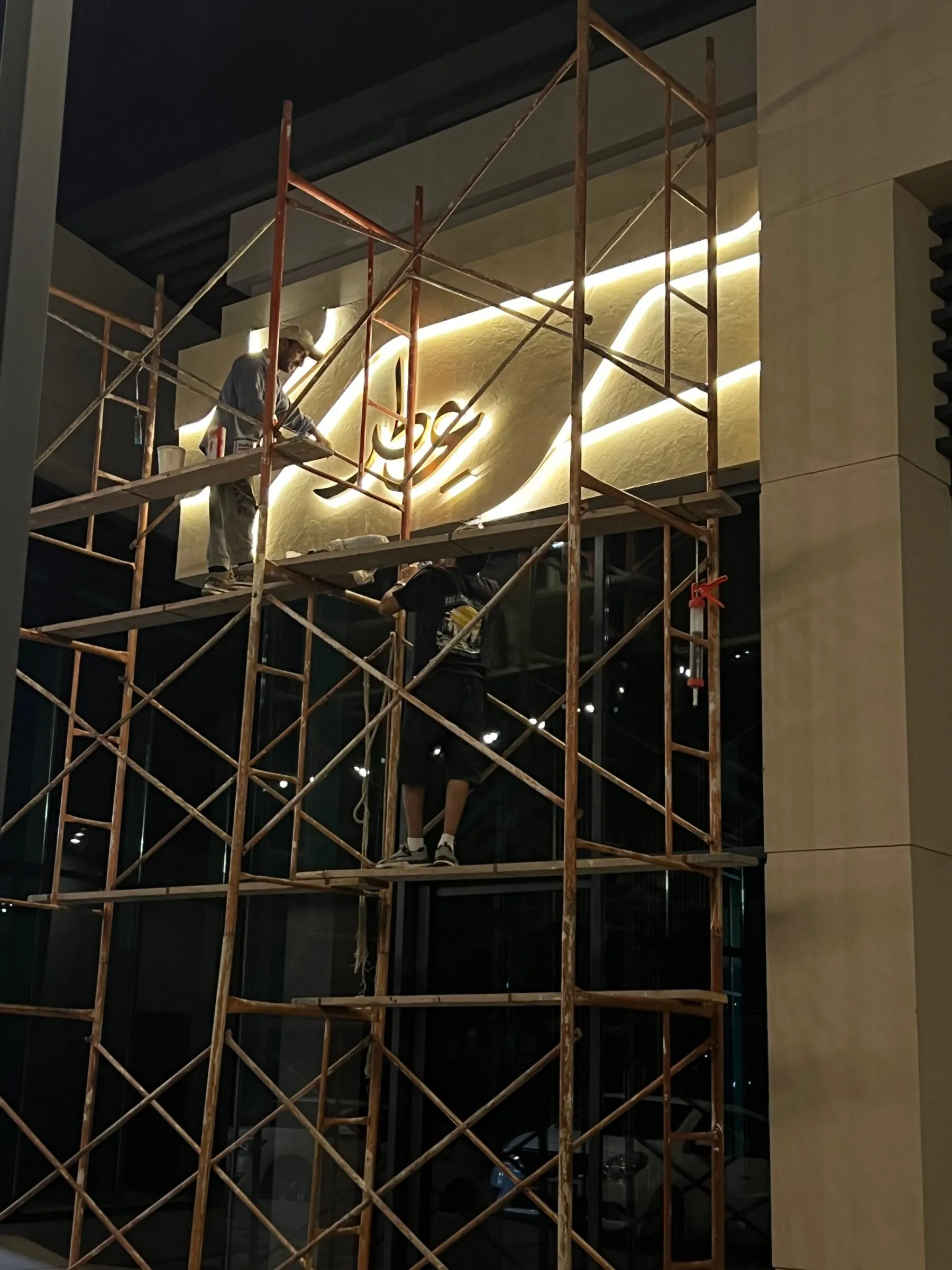 Night installation of the backlit signboard seen through scaffolding.