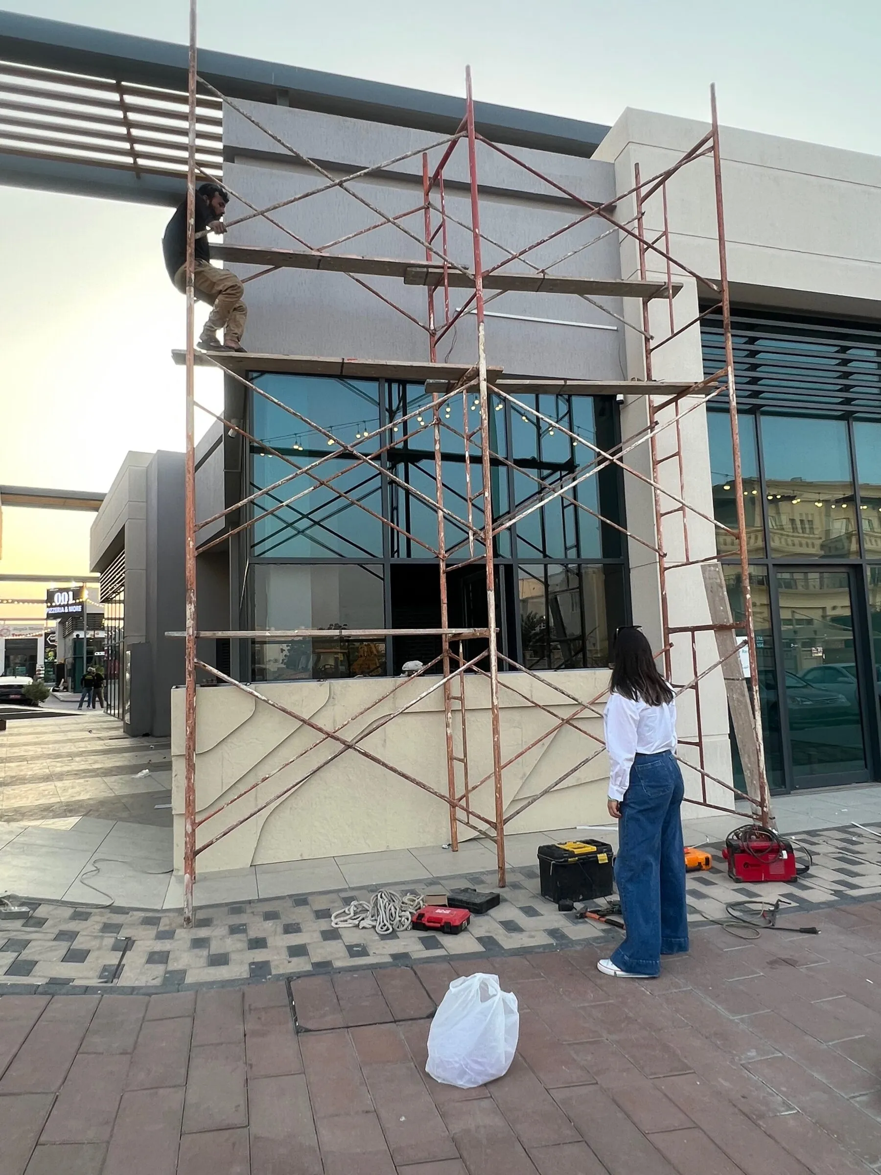 Shopfront wrapped in scaffolding during installation, with tools on the pavement.