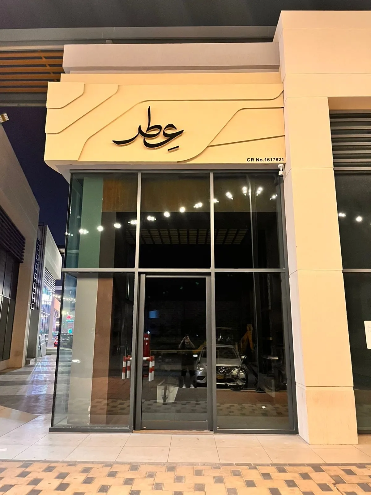 The finished storefront at dusk — a cream relief panel with a backlit Arabic calligraphic logo above a full-height glass shopfront.