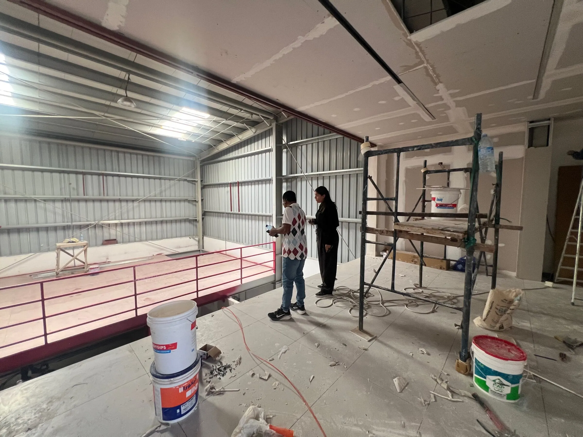 Site meeting on the mezzanine deck during construction, with paint and materials on the floor.